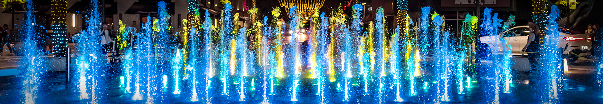 Centennial Square Fountain at night, water plumes glowing blue from dramatic uplights.