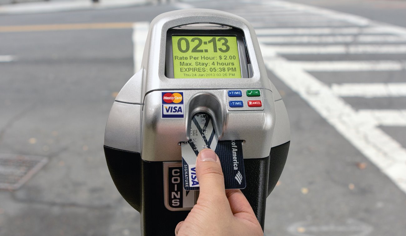 Credit card being inserted into solar-powered parking meter. 