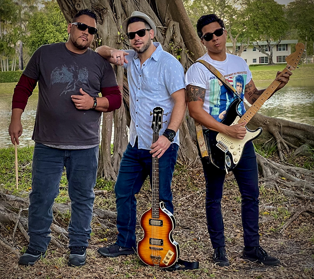 The male musicians wearing sunglasses, holding guitars, posed in front of large Banyan tree