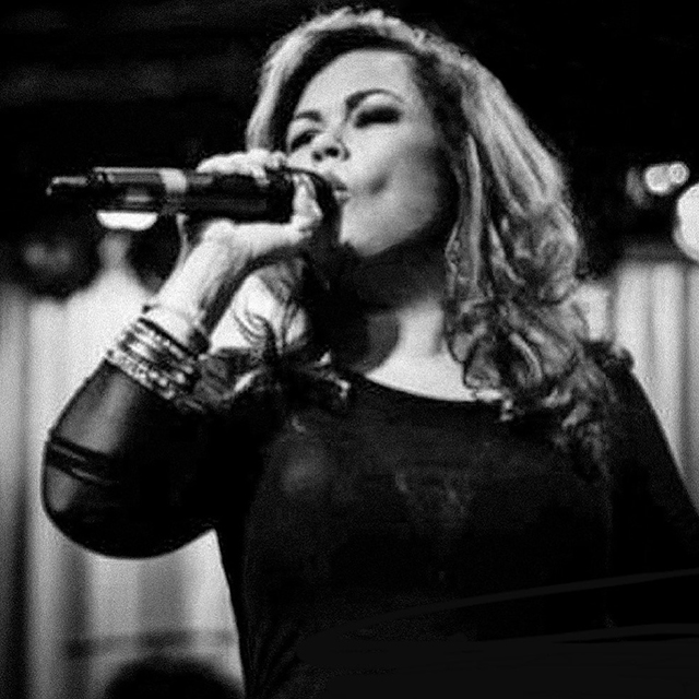 Black and white up-shot photo of Kim Lovering, of K-Luv and the United Funk Foundation, singing into a microphone.