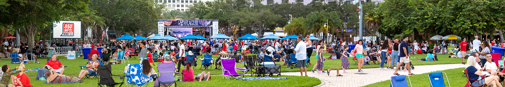 Pano of Waterfront Commons Great Lawn with stage in background, crowds of summer-dressed people relaxing, enjoying the event on a sunny day.