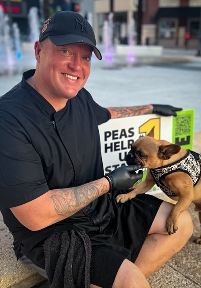 Chef Brett Portier kneels near Centennial Square fountain and smiles for the camera as he scratches a friendly French bulldog.