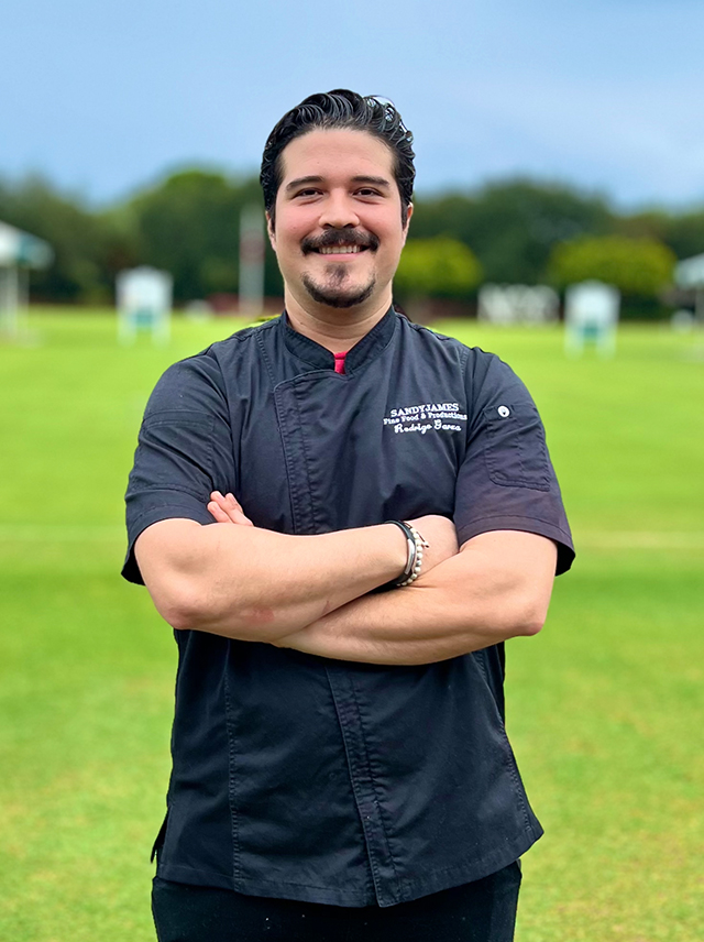 Portrait of Chef Rodrigo Cuevas against green lawn, blue sky.