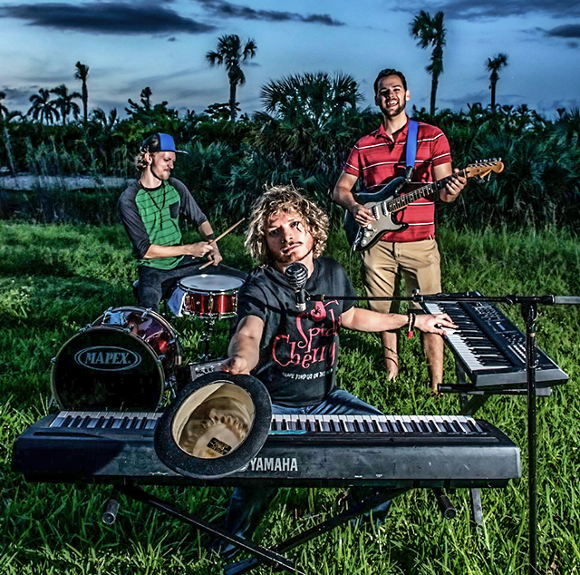 Three members of Spider Cherry band playing instruments in a South Florida grassy pasture at dusk.