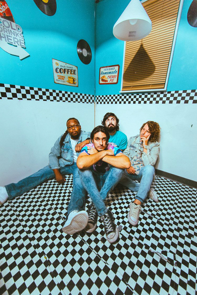 The East Harbor band posed seated on black & white checkered floor in retro-designed room