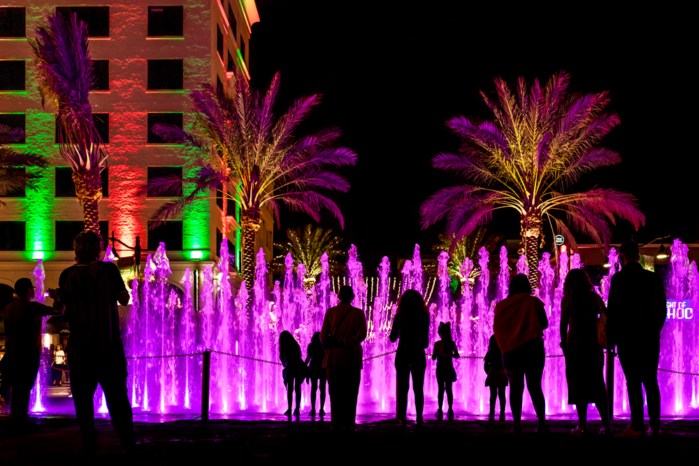 Photo of the fountain at Centennial Square park during night, lit in purple with people in silhouette.