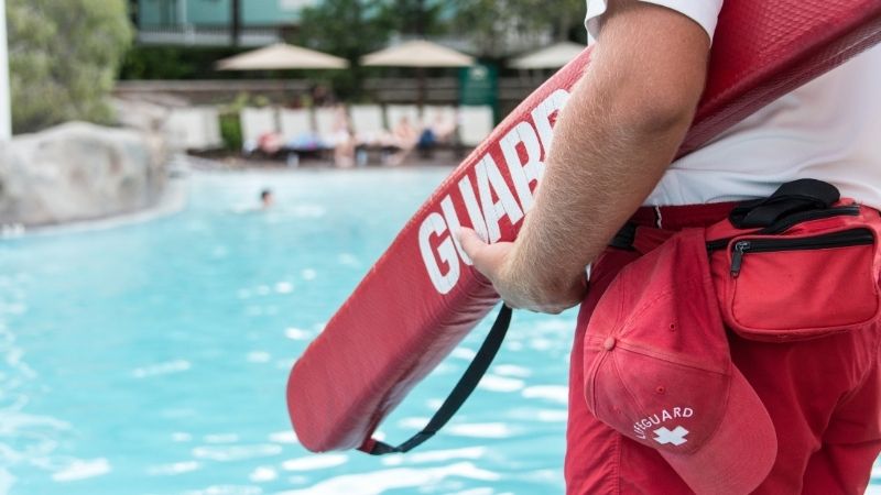 Image of a life guard holding a floating device near a pool