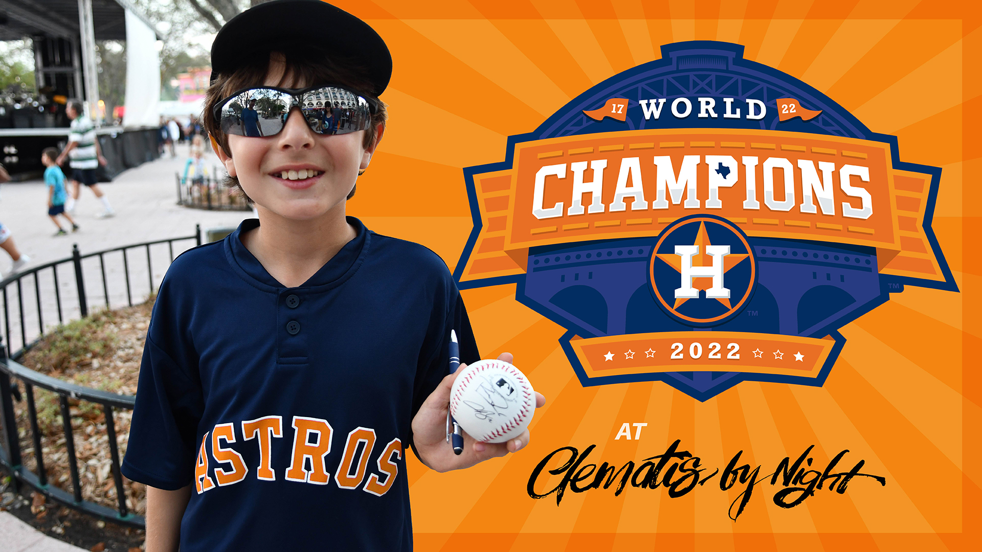 Smiling young boy in Houston Astros jersey holding up a signed baseball alongside Logo for World Champions Houston Astros 2022 at Clematis by Night